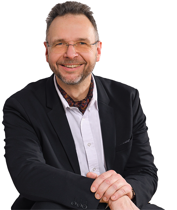 Portraitfoto von Sascha Kühnau. Freundlich grinsender Blick, leger getragener Anzug.