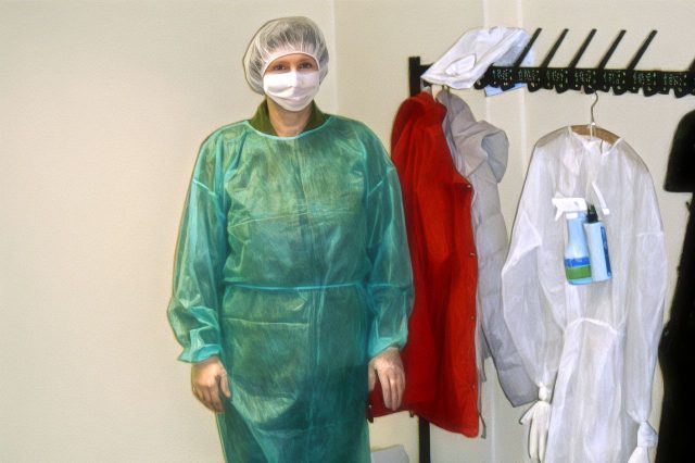 Eine Mitarbeiterin präsentiert in der Umkleide getragene Schutzausrüstung mit Anzug, Maske, Kopfhaube und Handschuhen, zum Umgang mit Infektionsfällen.