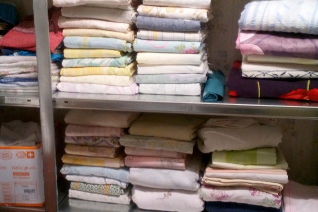 Regal mit sauber gefalteter Wäsche wie Bettlaken, Handtüchern und Textilien in verschiedenen Farben und Mustern, ordentlich gestapelt.